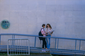 Photo of two young girls standing on a metal railing and discussing school subject