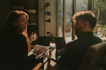Ginger female person explaining something to her male colleague while gesticulating with her hands