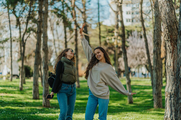 Fototapeta premium Lovely young girls, curly haired and brunette, posing for the camera while hanging out in the park on a beautiful sunny day