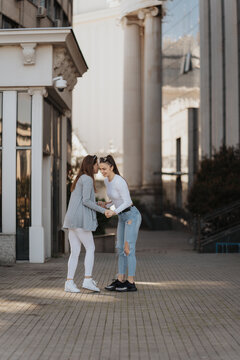 Photo of two young women enjoying a sunny day and having a conversation on the city sidewalk