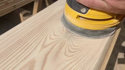 The man holding a grinder tool. With a special nozzle with sandpaper, which is fixed in the grinder tool, they grind a wooden surface.