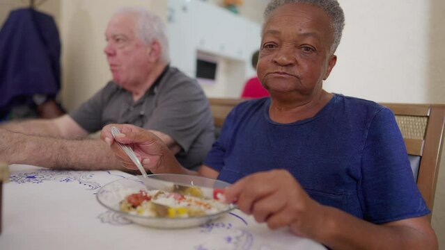 African American senior woman eating lunch with friends, diverse scene of elderly people gathered for lunch, candid and authentic