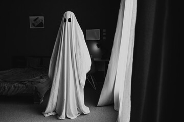 Black and white photo of ghost covered with a white ghost sheet in the room at home. Halloween Concept