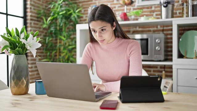 Young beautiful hispanic woman using laptop and touchpad sitting on table at dinning room