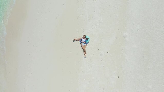 Aerial top view of happy couple in love on the white sand beach with turquoise water sea in Thinadhoo island, Maldives.
