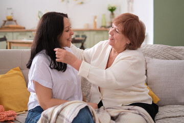 Heartwarming moment between a mother and her grown-up daughter as they chat and laugh on a couch. Family gatherings and how to create a warm and welcoming atmosphere