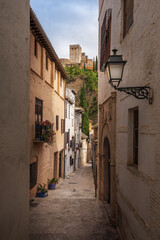 Street of traditional Albaicin district with Alhambra Towers on background - Granada, Andalusia, Spain