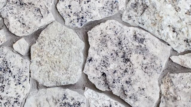 Background, masonry wall of stones of different irregular shapes on cement mortar, rotating, turning, close-up 
