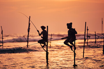Silhouettes of two traditional fishermen against ocean at dusk. Traditional stilt fishing near...