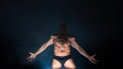 Obraz premium Muscular athlete in an epic pose, dark background, bright light from below, the concept of sports and bodybuilding