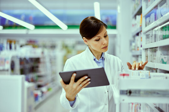 A Serious Female Pharmacist Checking The Expiration Date Of A Medicine Box.