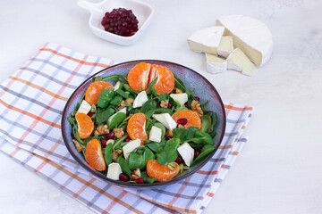 Tangerine salad with mixed leaves, Camambert and walnuts in a grey bowl on cotton chessboard pattern napkin. Placed on white background