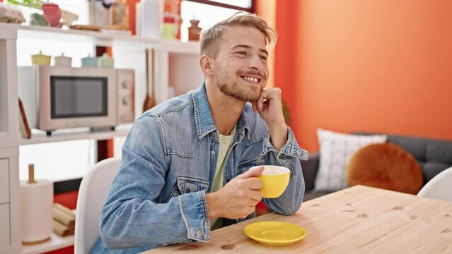Young caucasian man holding cup of coffee sitting on table at dinning room