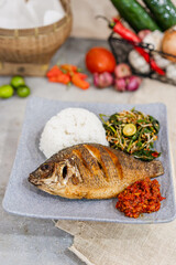 Ikan Gurami Goreng Lalapan or Fried Gurami Fish, One of Indonesia's culinary icons on decorated background with rice and vegetables