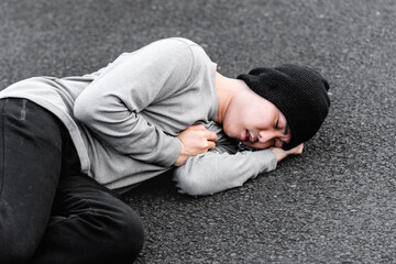 Asian young man lying on the ground, hand covering his heart, concept of sudden heart attack or...