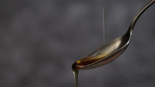 Maple syrup being dropped onto a teaspoon in slow motion against a dark gray background