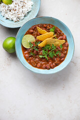 Turquoise bowl with chilli con carne or spicy meat stew served with rice and nachos, top view on a light-beige stone background, vertical shot, copy space