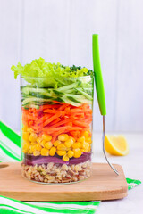 Healthy salad with bulgur and vegetables in mason jar on wooden board with with fork. White background. Side view