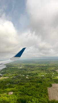 Airplane flies low over a lush green landscape, descending to land on the airport landing strip at Gerald Ford International Airport in Grand Rapids, Michigan, USA. Passenger point of view.