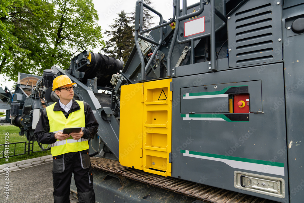 Poster engineer with digital tablet next to road construction machine..