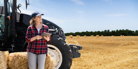 Woman farmer with a digital tablet next to agricultural tractor