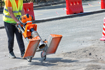 A road worker pulls a petrol drill to cut asphalt concrete samples.