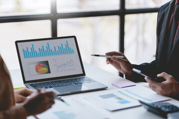 Meeting of business people pointing at graphs and charts to analyze market data. Group of businesspeople meeting together analyzing and pointing laptop about business growth.