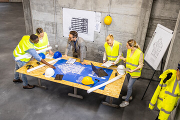 Top view of contractor and architects analyzing plans and blueprints of the new project at...