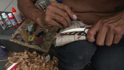 on the street man with beard of Indian appearance first people of Canada locals carving feather Poor people poverty close-up details of his work sawdust hands creativity crafting Vancouver Canada 2023