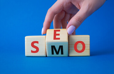 SEO vs SMO symbol. Businessman hand turns wooden cubes and changes the word SMO to SEO. Beautiful blue background. SEO vs SMO and business concept. Copy space