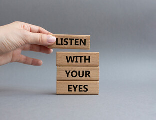 Listen with your eyes symbol. Concept word Listen with your eyes on wooden blocks. Beautiful grey background. Businessman hand. Business and Listen with your eyes concept. Copy space