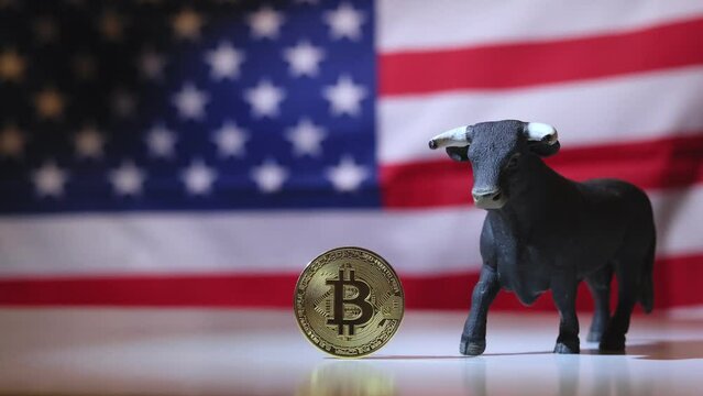Physical Bitcoin coin and a bull figurine placed in the center of the frame with an American flag waving in the background. This composition symbolizes a bullish market trend in the world of cryptocur