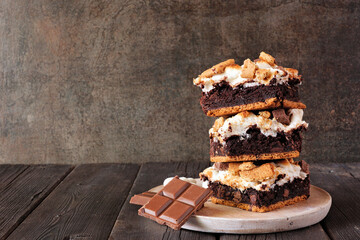 Stack of smores brownie dessert bars. Side view table scene with a dark background.