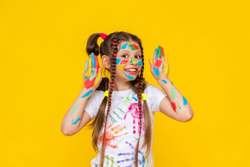 A young girl with brightly painted hands and multi colored pigtails shows her palms, smiling broadly. Yellow isolated background.