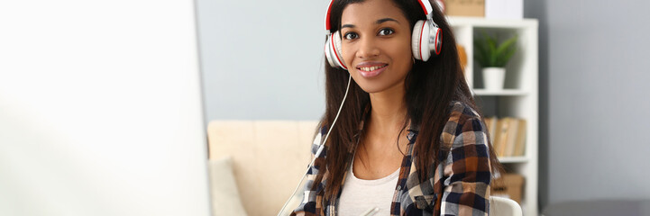African female student wears headphones studying alone at home office desk. Mixed race woman...
