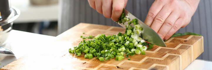 Closeup of hands of cook holding knife for cutting green onions. Sliced fresh green onions and...