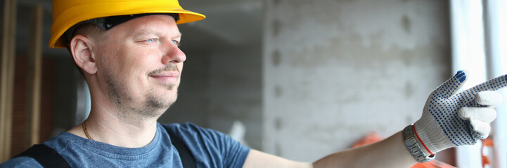 Male builder in helmet looks out window at construction site. Foreman foreman and foreman of construction projects concept