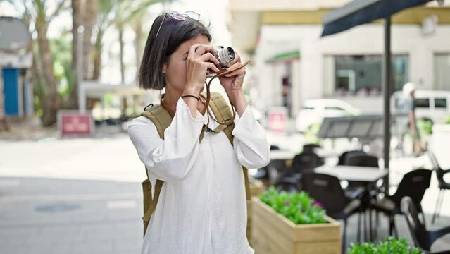 Young beautiful hispanic woman tourist smiling confident using vintage camera at coffee shop terrace