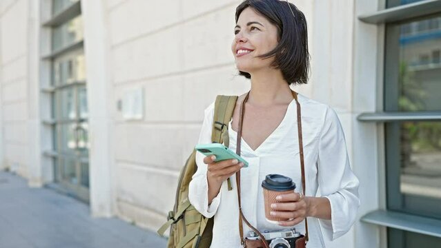 Young beautiful hispanic woman tourist smiling confident using smartphone drinking coffee at street