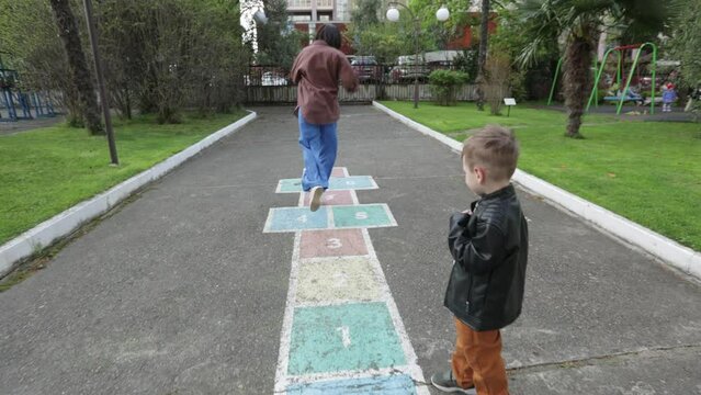 Mom teaches son jump on painted hopscotch