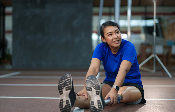 Athlete using a prosthetic leg warming up at the Gym. Woman relaxing and streching while using prosthetic equipment. Close up a woman with a leg prosthetic..