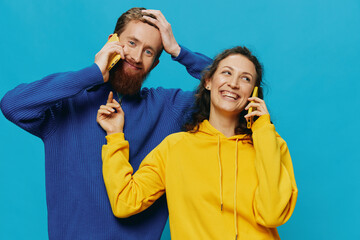 Obraz premium Woman and man cheerful couple with phones in their hands crooked smile cheerful, on blue background. The concept of real family relationships, talking on the phone, work online.