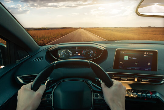 Driving car through a perfect road. Fields illuminated by sunrays. First person view. Modern car with displays on dashboard