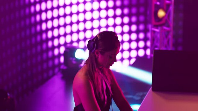 Portrait of attractive female techno DJ performing playing her music set on a stage of a nightclub or during a festival