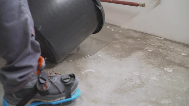 A male worker working with self-levelling cement mortar during a floor repair. A worker pours a bucket of mortar to level the floor. Self-levelling concrete floor mix.