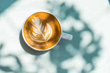Top view of cup of tasty cappuccino with latte art on blue background with shadows at sunny day outdoor.