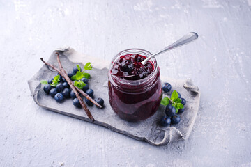Reife Blaubeeren aus biologischem Anbau und Marmelade mit einer Vanille Schote als Nahaufnahme auf einem grauen Design Tablett mit Textfreiraum