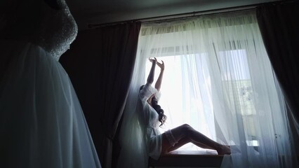 Close up shot of a sexy bride in petticoat putting on a garter near a window