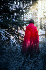 A woman in a red cloak escaping through the forest in winter. 