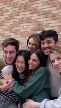 Happy group of young students hugging each other laughing outdoors. Friendly group of millennial friends having fun together at city street. Vertical video.